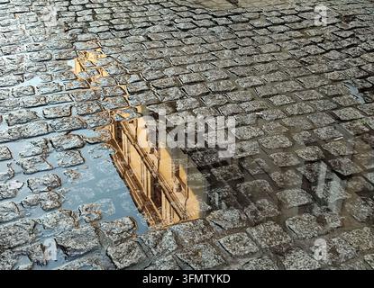 Historisches Gebäude, das sich in einer Regenpfütze auf einer traditionellen Kopfsteinpflasterstraße in Krakau, Polen, spiegelt. Stockfoto