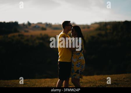 Romantisches Paar, das sich in einer ländlichen Feldlandschaft zur Goldenen Stunde umarmt und küsst Stockfoto