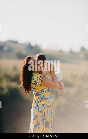 Mutter küsst und hält ihre kleine Tochter im sonnigen Landschaftsgebiet und umarmt die Liebe Stockfoto