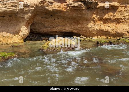natürliche Meereshöhle unter Sandsteinklippen mit sanften Wellen, die über felsige Formationen entlang einer mediterranen Küste in Spanien spülen Stockfoto