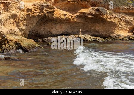 sanfte Wellen, die über felsige Küstenlinie unter rauen mediterranen Klippen schwappen, und die natürliche Küstenerosion und Meeresküstenlandschaft in Spanien zeigen. Stockfoto