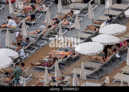 Luftbild von Menschen, die auf Liegestühlen unter weißen Sonnenschirmen am Kiesstrand in Nizza, Provence-Alpes-Côte d'Azur, Frankreich entspannen Stockfoto