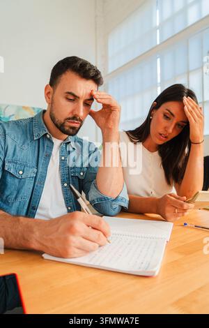 Zwei Personen sitzen an einem Holztisch gegenüber, einer schreibt in ein Notizbuch, während der andere mit einem nachdenklichen Blick nach vorne lehnt, was Zusammenarbeit und Stockfoto