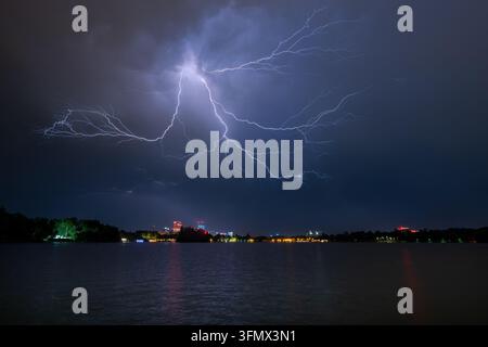 Blick auf einen mächtigen Blitzschlag, der den Nachthimmel über der Stadt Skyline und dem See in Bukarest, Bukarest, Rumänien, erhellt Stockfoto