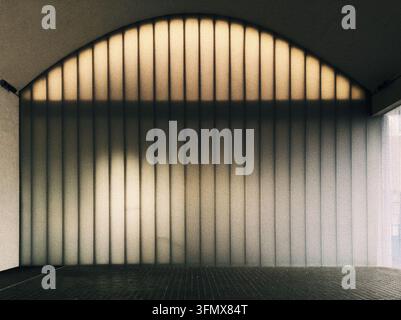 Minimalistische Aufnahme einer massiven durchscheinenden gerippten Wand, die einen großen Torbogen bildet, wunderschön mit warmem Licht hinterleuchtet, das durch die Textur filtert. Stockfoto