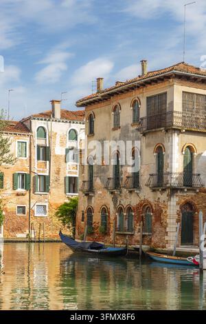 Ansicht einer traditionellen Gondel, die an einem ruhigen Kanal vor historischen Backsteingebäuden mit grünen Fensterläden in Venedig, Veneto, Italien, festgemacht ist. Stockfoto
