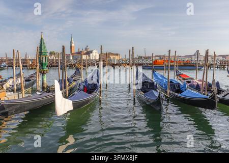 Blick auf Gondeln, die an Holzpfählen in der Lagune von Venedig festgemacht sind, mit der historischen Skyline von Venedig im Hintergrund unter einem klaren blauen Himmel, Venedig, V Stockfoto