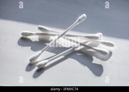 Ein kleiner Haufen weißer Wattestäbchen ruht auf einer neutralen Oberfläche, die von direktem Sonnenlicht beleuchtet wird und deutliche dunkle geometrische Schatten wirft. Das hygienische Kinderbett Stockfoto