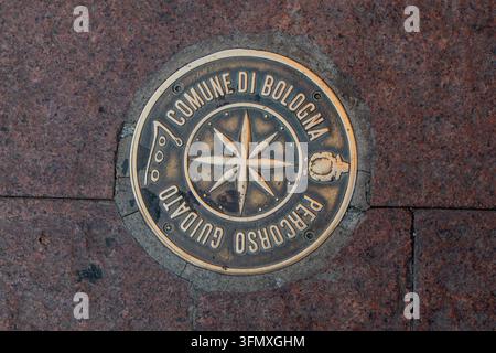 Bologna, Italien, 3. August 2026. Eine von oben nahe Aufnahmeshot einer runden Messing-Gedenkplakette, die in einen roten Granitstein-Pflasterweg eingelassen ist Stockfoto