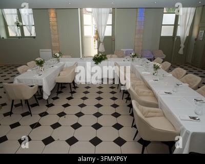 Essbereich im Innenraum mit für eine Veranstaltung gedeckten Tischen, mit beigen Stühlen und geometrisch gefließtem Boden. Stockfoto
