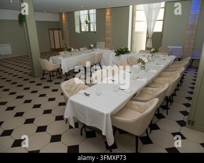 Interieur eines leeren Speisesaals mit weißen Tischdecken, beigen Stühlen und floralen Tafelaufsätzen. Stockfoto