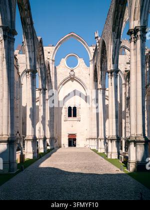 Sonnenbeschienene Ansicht durch hoch aufragende gotische Bögen bei den Ruinen des Karmeliterklosters in Lisboa, Portugal, die das offene Dach, Steinsäulen, das historische Langhaus und klares Licht offenbaren Stockfoto