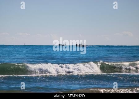 Brachende Meereswellen mit weißem Schaum rollen unter einem klaren blauen Himmel auf das Ufer zu. Stockfoto