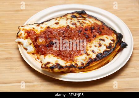 Nahaufnahme von gebackener italienischer Lasagne, geschichtet mit Pasta, reichhaltiger Tomatensauce und geschmolzenem Käse, serviert auf einem weißen Teller über einem rustikalen Holztisch. Stockfoto