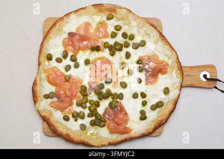 Ansicht von oben einer italienischen Pizza mit geräuchertem Lachs, Kapern und geschmolzenem Käse auf einem Holzschieber, die mediterrane Küche und hausgemachte Gastronomie präsentiert Stockfoto