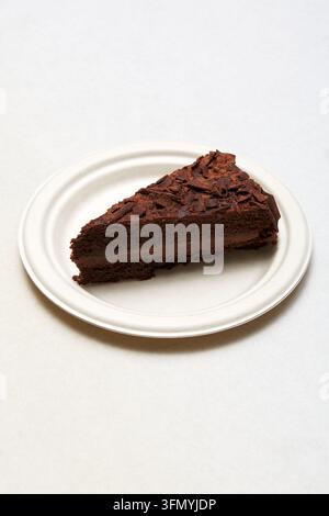 Ein reichhaltiges Stück italienischer Schokoladenkuchen mit cremiger Füllung und Schokoladenraspeln ruht auf einem weißen Teller vor einem sauberen, hellen Hintergrund. Stockfoto