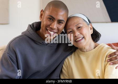 Senior asiatische Mutter und Sohn sitzen auf dem Wohnzimmersofa, lehnen sich vor, gelber Pullover, grauer Hoodie Stockfoto