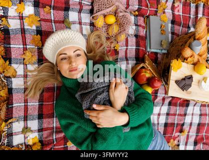 Frau breitet Picknickdecke auf Herbstblättern im Park aus Stockfoto