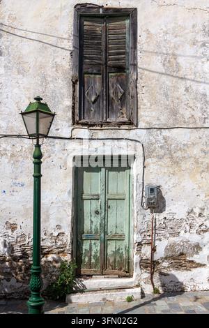 Verwitterte grüne Holztür und Fensterläden an einem alten weiß getünchten Haus in Fournoi, Griechenland, Europa, neben einer traditionellen Straßenlaterne und abblätterndem Putz Stockfoto
