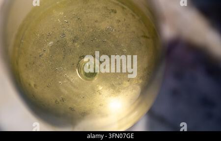 Eine Makro-Aufnahme von oben, die ein dichtes Klumpen winziger Luftblasen und Flüssigkeitstexturen in einem runden Glas mit frischem Weißwein einfängt, hochl Stockfoto