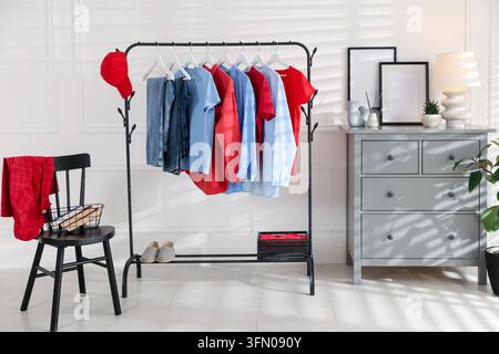 Verschiedene Kleidungsstücke hängen an einem Kleiderständer, Baseballkappe und Schuhe drinnen Stockfoto