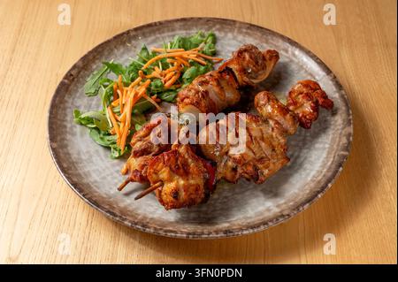 Gegrillte Fleischspieße serviert mit frischem Salat und Gemüse auf einem rustikalen Keramteller auf einem Holztisch Stockfoto
