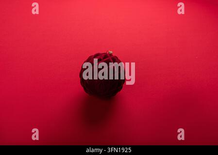 Einziger tiefroter Weihnachtsanhänger aus Samt mit gesteppter Textur und dezentem Glanz. Isoliert auf einem nahtlosen lebhaften roten Hintergrund mit weichem Schatten. S Stockfoto