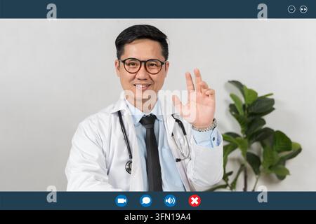 Lächelnder Arzt winkt zur Begrüßung, trägt weißen Kittel und Stethoskop. Grüne Pflanze im Hintergrund verleiht der Szene Ruhe. Ideal für Gesundheitswesen, medizinische Dienstleistungen Stockfoto