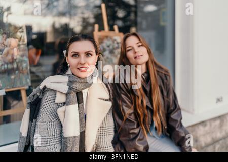 Freundinnen Kunst zwei junge Frauen sitzen zusammen vor einer Kunstgalerie und genießen einen sonnigen Herbsttag in der Stadt Stockfoto