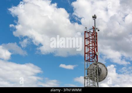 Roter und weißer Kommunikationsmast mit großer Satellitenschüssel unter bewölktem Himmel Stockfoto