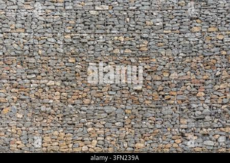 Steinerne Umzäunung aus kleinen unregelmäßigen grauen und beigen Steinen, die eine raue, texturierte Oberfläche mit einem sich wiederholenden Naturmuster bilden Stockfoto