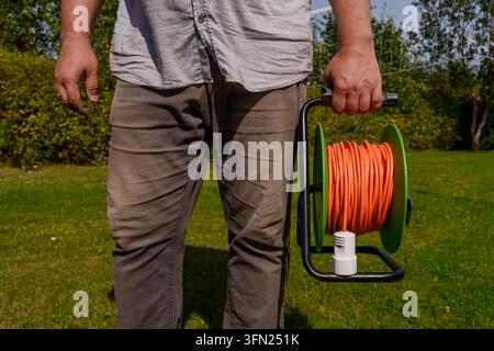 Mann hält eine orangefarbene elektrische Verlängerungskabelrolle im Garten Stockfoto