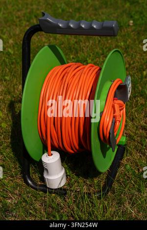 Orange Verlängerungskabelspool auf grünem Gras im Garten Stockfoto