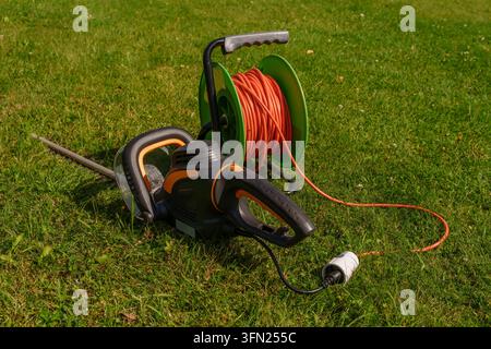Elektrischer Heckenschneider mit Verlängerungskabelspool auf grünem Gras Stockfoto