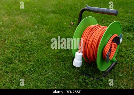 Orange Verlängerungskabelspool auf grünem Gras im Garten Stockfoto