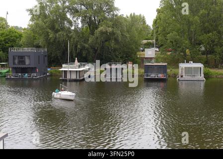 Menschen in einem kleinen Boot, das an den ehemaligen Docks der Moldau angebundene Hausboote passiert, Prag, Tschechische Republik, Juni 2026 Stockfoto