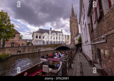 BRÜGGE, BELGIEN, 15. JULI 2025 - Die historischen Kanäle von Brügge, Belgien, mit dem Turm der Kirche Unserer Lieben Frau im Hintergrund und den Pier-Touren Stockfoto
