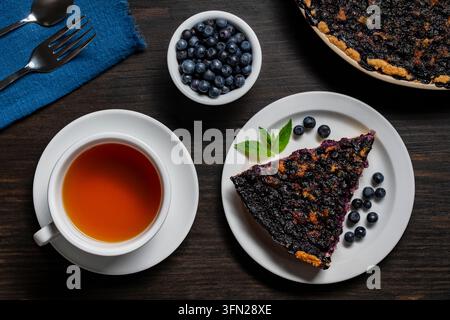 Scheibe hausgemachter Blaubeerkuchen mit einer Tasse Tee, Nahaufnahme. Blick von oben auf eine köstliche Scheibe Blaubeerkuchen, serviert mit einer Tasse heißem Tee und frischen Beeren Stockfoto