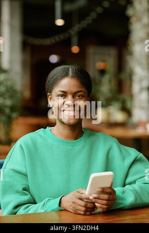 Porträt einer lächelnden schwarzen Frau, die im Café ein Smartphone hält Stockfoto