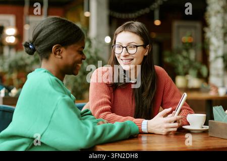 Verschiedene Freundinnen, die an einem Cafétisch sitzen und ein Smartphone benutzen Stockfoto