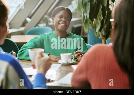 Fröhliche schwarze Frau lacht mit verschiedenen Freunden am Café-Tisch Stockfoto