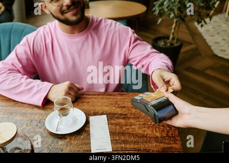 Mann, der eine Rechnung mit Kreditkarte an einem POS-Terminal im Café bezahlt Stockfoto
