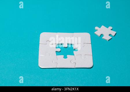 Weißes Puzzle-Set mit einem fehlenden Teil in der Mitte, isoliert auf hellem zyanfarbenem Hintergrund, das Geschäftsstrategie, Lösung und Erfolg im Teamwork darstellt. Hochwertiges Foto Stockfoto