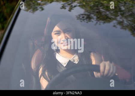 Glückliche junge asiatische Frau, die auf dem Fahrersitz sitzt und ein modernes Auto lenkt. Stockfoto