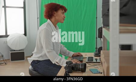 Frau, die auf der Tastatur neben einer dslr-Kamera auf dem Tisch im Studio tippt, mit Monitor und Bedienfeld für Bearbeitung und Farbabstufung; kreatives Konzentrieren Stockfoto