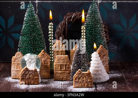 Ein Dorf aus Lebkuchenhäusern, dekorative Tannenbäume, Kerzen und ein Kranz davor. Stockfoto