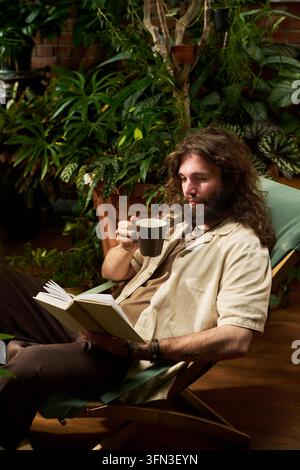 Mann liest ein Buch und trinkt Kaffee in einem Indoor-Garten Stockfoto