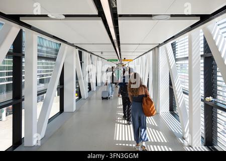 London, England, Vereinigtes Königreich, 12. August 2026. Passagiere gehen mit Gepäck durch einen gläsernen Korridor am Flughafen Heathrow in Richtung der Ankunftshalle Stockfoto