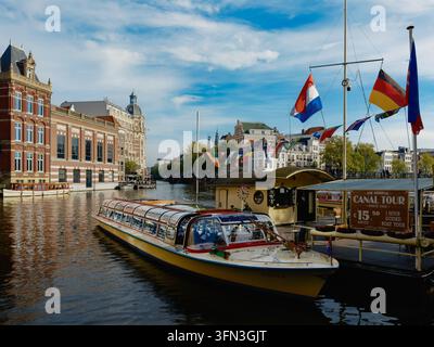 Rederij P. Kooij Rondvaart-Kanalrundfahrt-Boot, das am Amstel-Fluss unter niederländischen und internationalen Flaggen im Zentrum von Amsterdam, Niederlande, angelegt ist Stockfoto
