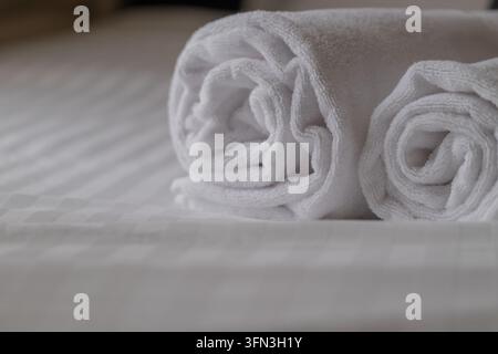 Gerollte weiße Handtücher auf dem Bett im Hotelzimmer Stockfoto